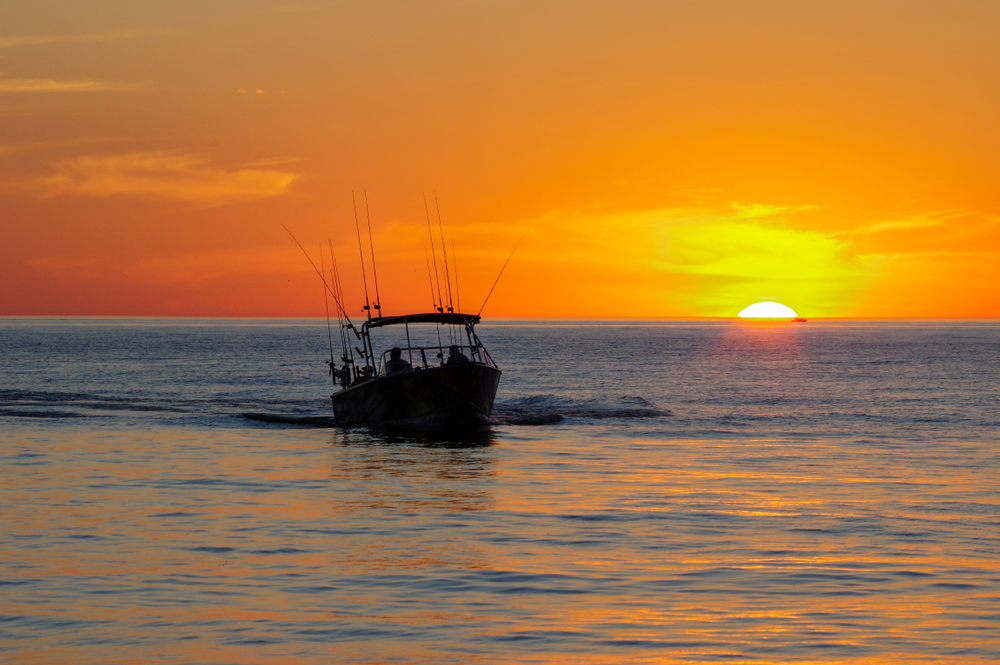 Silhouette of a boat with fishing poles against an orange sunset.