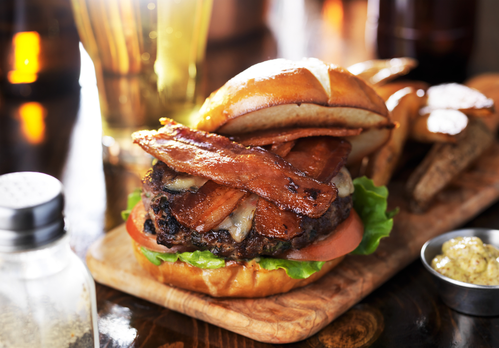 A bacon cheeseburger with a pretzel bun with a side of fries.