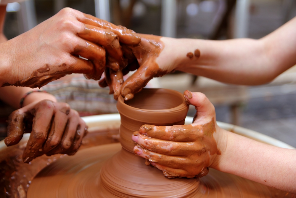 A couple's hand work to form clay on a spinning wheel.
