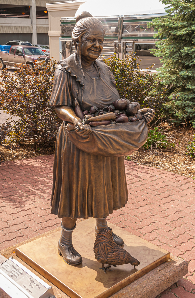 A sculpture of an old woman with an apron full of fresh vegetables and a chicken at her feet.
