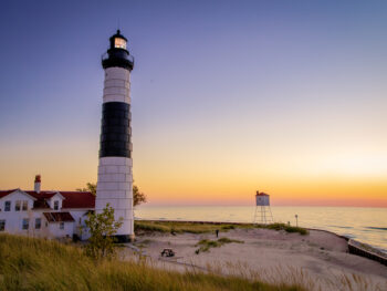 Black and white lighthouse with brilliant yellow sunset in background. beach towns in Michigan