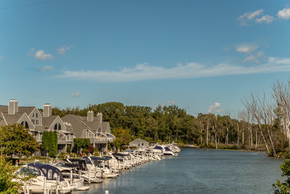 Boats in focus in front of beautiful townhomes in the lovely beach and harbor area. It is surrounded by trees. 