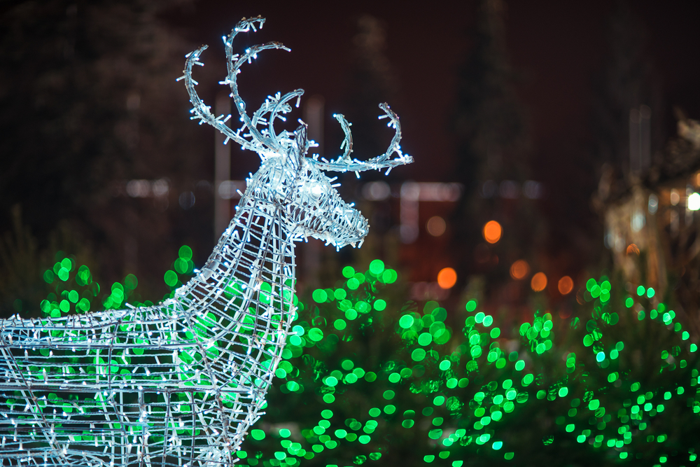 A silver deer made of twinkling lights with green lights in a shrub behind it