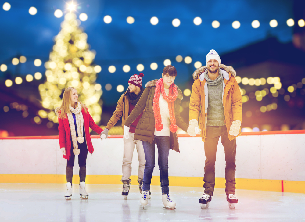 Two couple ice skating outside in a rink surrounded by twinkling lights during Christmas in Branson