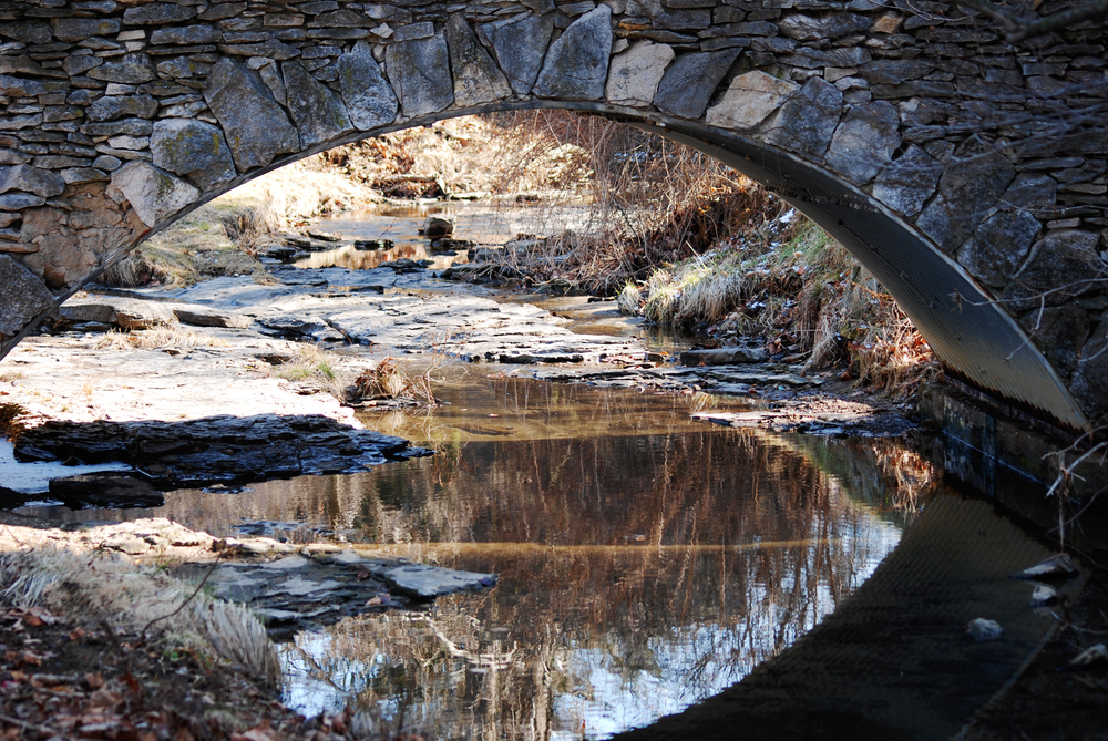 A stone bridge that goes over a small creek that has more stones in it in the middle of the winter