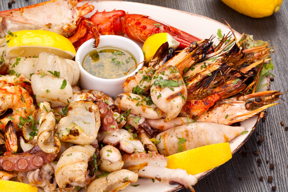 Seafood platter containing all different types of seafood with lemins and an oil dip. 