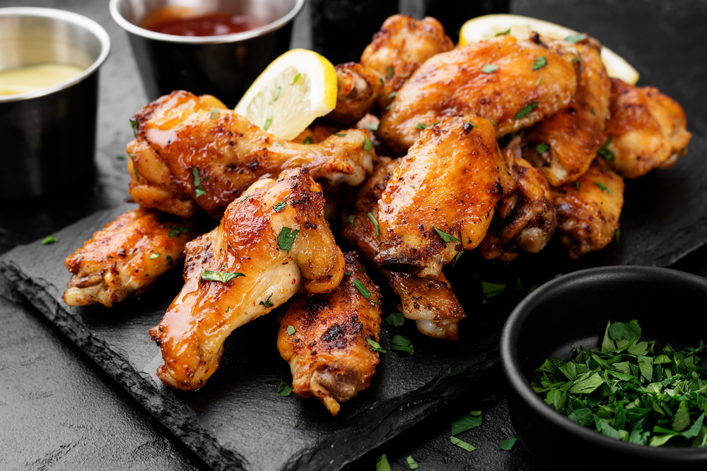 Baked chicken wings served with different sauces and lemon. They are on a piece of slate 