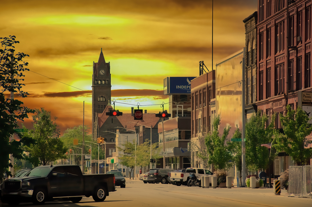 Golden sunrise in the city of Bay City Michigan in an article about restaurants in Bay City. You can see buildings and cars on the street. 