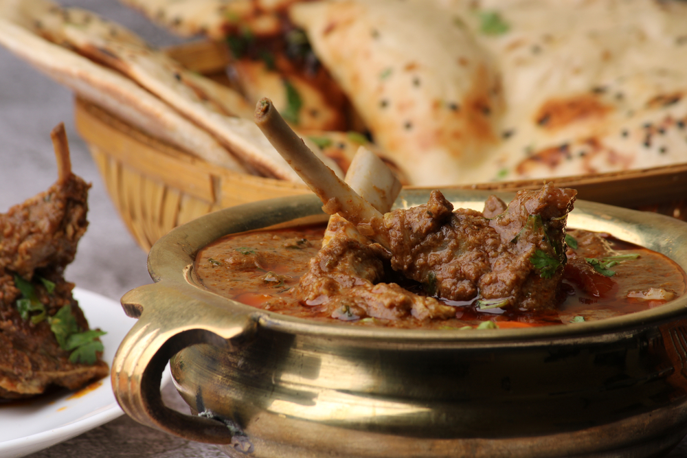 lamb bhuna in a metal serving dish  with naan bread in the background. 