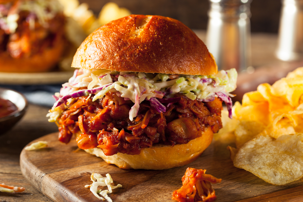 Pork Slider - pork in a bun with coleslaw. It sits on a wooden board with a side of crisps 