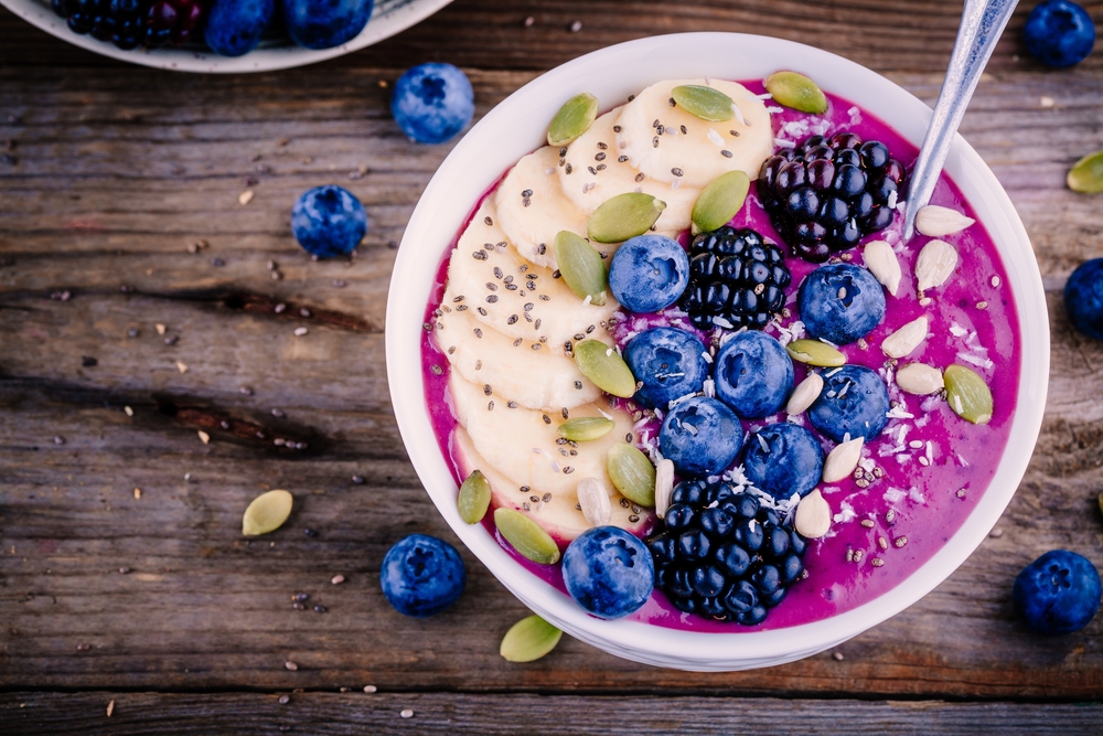 Purple smoothie bowl with fresh blackberries, blueberries, banana, sunflower seeds, pumpkin seeds, chia seeds and coconut