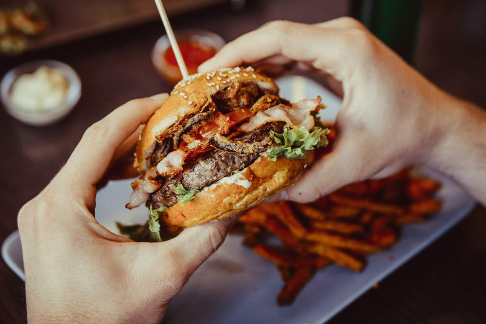 man holds burger with hands with fries and dips on background in an article but restaurants in Soiux Falls 