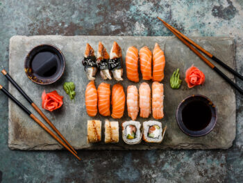An overhead view of a platter of sushi and sashimi rolls with soy sauce, pickled ginger, wasabi, and two sets of chopsticks. Its similar to what you can find at sushi restaurants in Pierre.