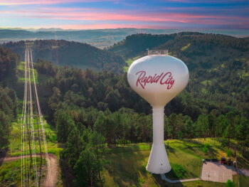 Overhead view of silver water tower with red letters Rapid City surrounded by greenery. Attraction in Rapid City