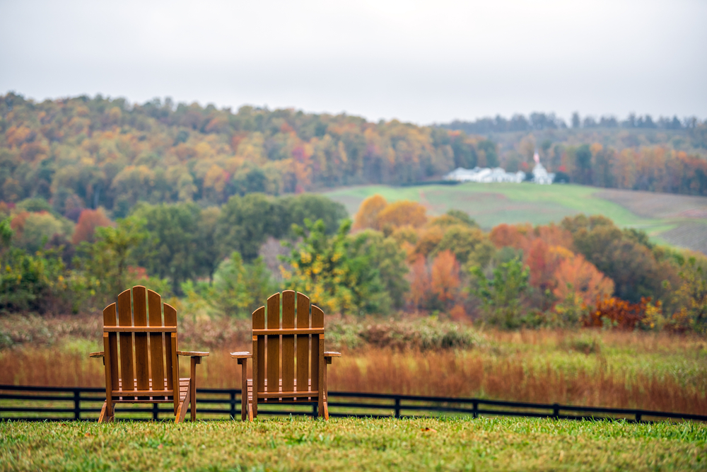 Two Adirondack chairs on the side of a hill looking out towards a winery in Missouri on a fall day. 