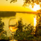 A glass of white wine with a river in the background as the sun is setting, similar to what you'd find at wineries in Missouri.