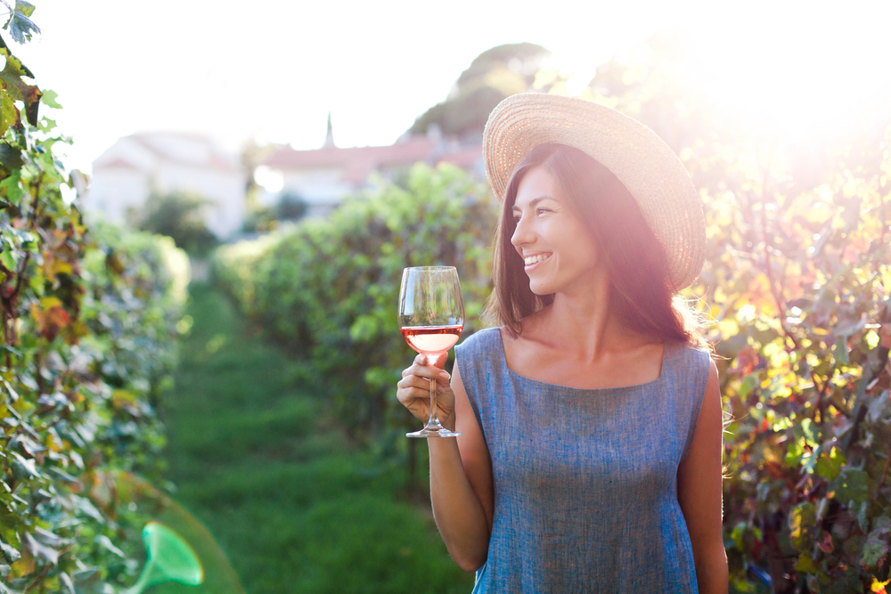 A woman in a wide brimmed hat holding a glass of wine in a vineyard as the sun sets, similar to what you'd find at wineries in Missouri