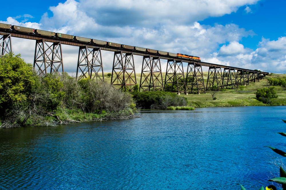 A train going over an old bridge and bright, blue water.