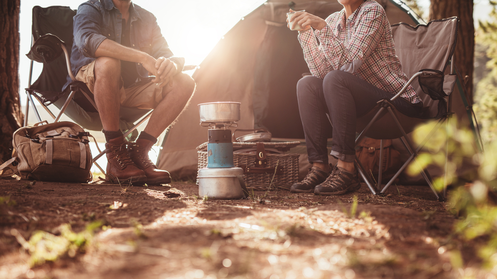 Cropped image of man and woman sitting in chairs outside the tent. Couple camping in forest. Aricle is about camping in North Dakota 