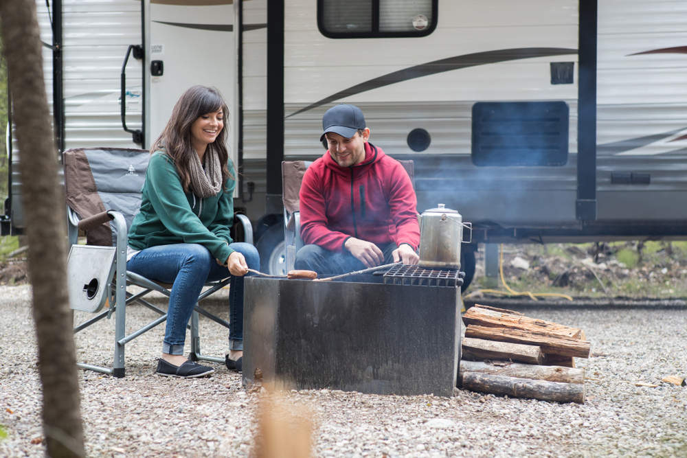 A young  couple relaxing at their camp site while RV camping, They are grilling outside their RV 