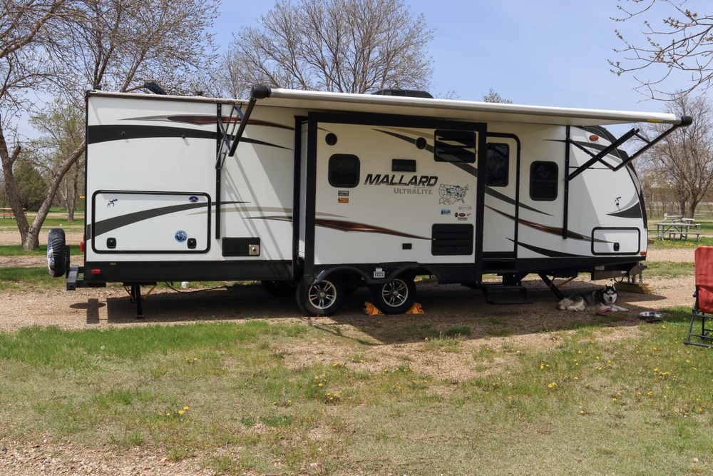 Camper set up at campground. The camper is large and white and is on a hard standing surrounded by grass. In an article about camping in North Dakota 