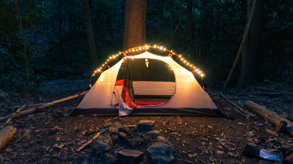 camping tent in the forest with fairy lights. Campfire, axe, backpack and blanket