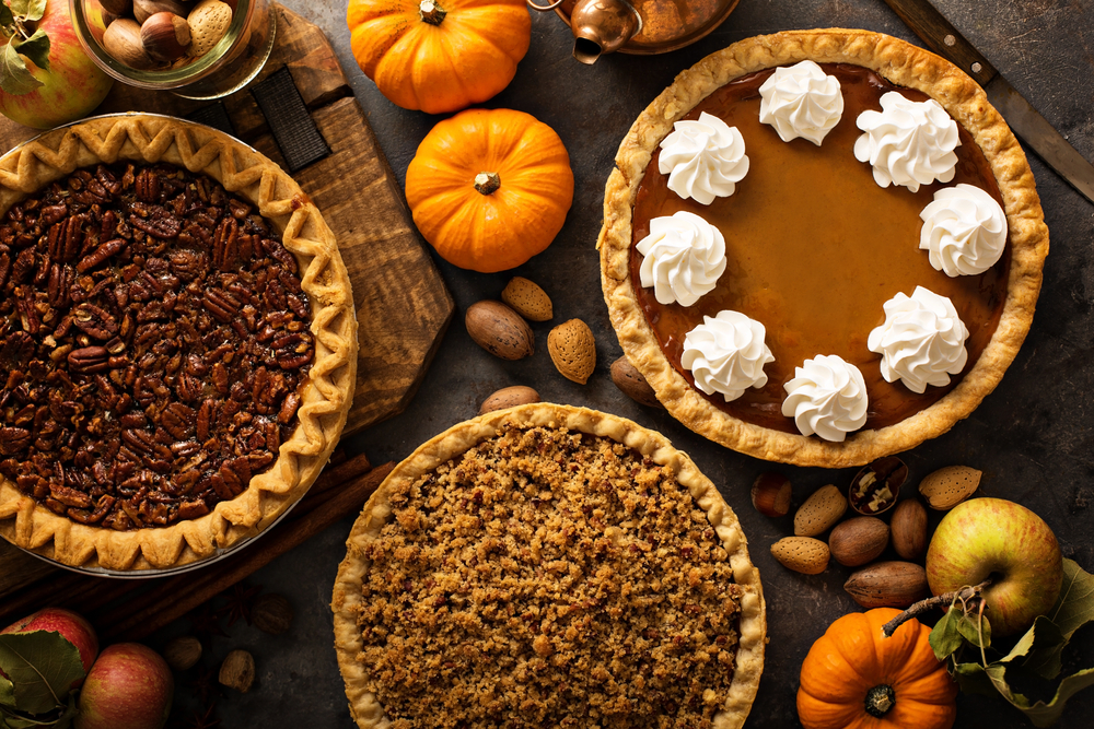 A pecan, apple, and pumpkin pie on a table with small pumpkins and pecans on it. 