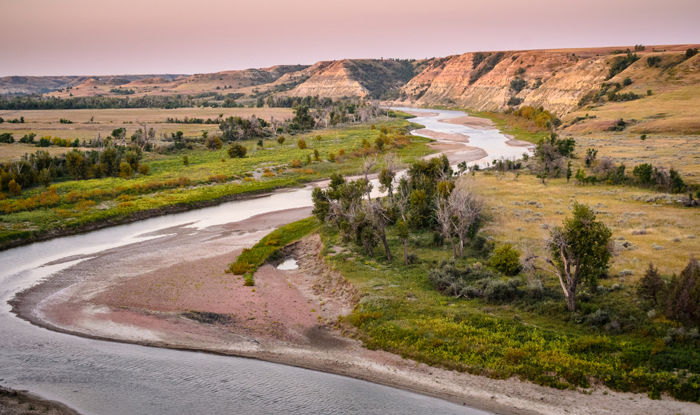 Theodore Roosevelt National Park, North Dakota. One of the places to go hiking in North Dakota. the pictures shows a river cutting through a dry valley.  