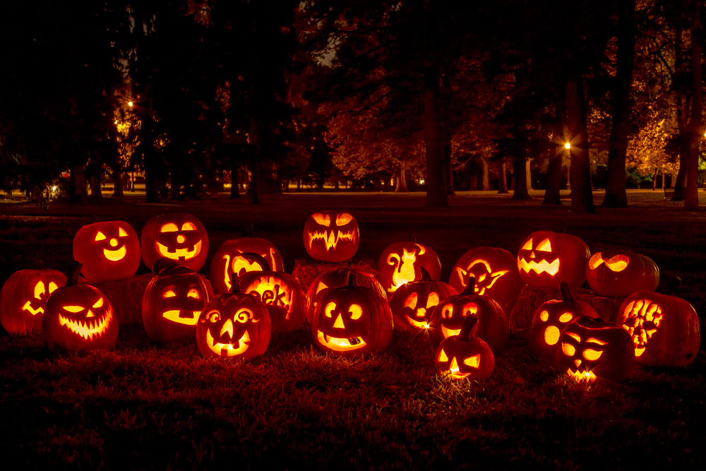 A group of jack-o-lanterns lit up at night. They all have different carvings. 