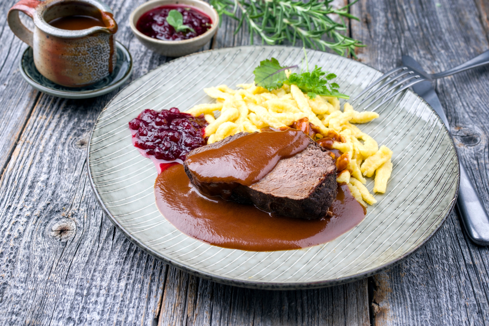 Traditional braised marinated German Sauerbraten from beef with spaetzle and cranberry jam in spicy brown sauce as closeup in a modern design plate