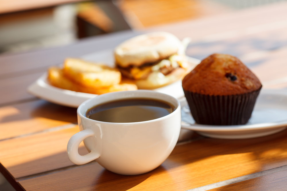 A coffee muffin and breakfast sandwich on a table in a cafe.  