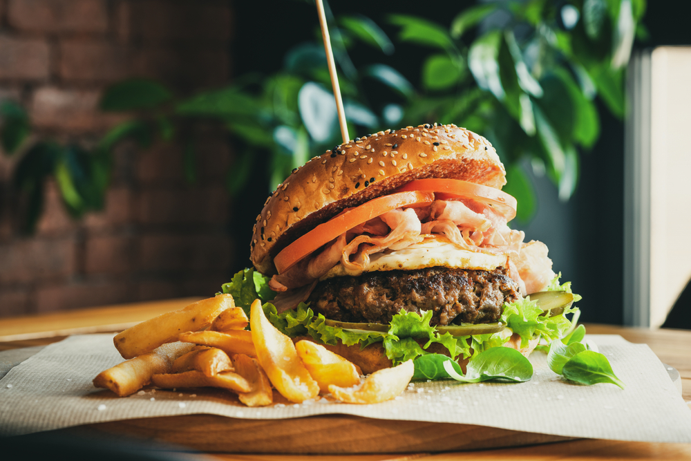 Beef Egg and Bacon Burger Served in Restaurant. there is a side of freid and its on a wooden table. One of the restaurants in Evansville 