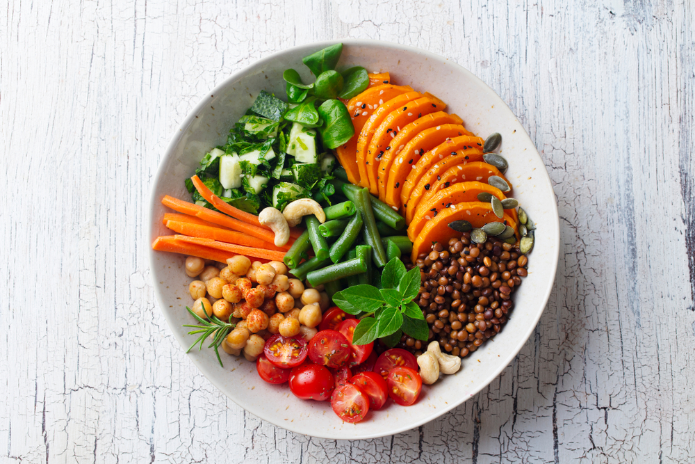 Top view of a healthy vegetarian salad. Lentil, chickpea, carrot, pumpkin, tomatoes, cucumber. The bowl is on a wooden backdrop in an article about restaurants in Evansville  