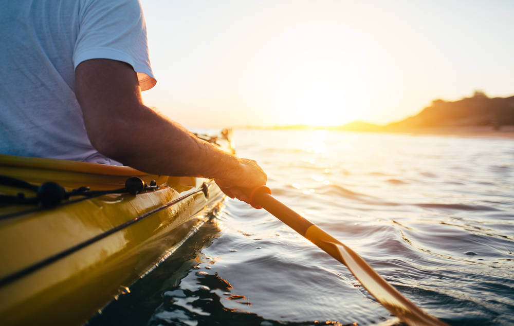 Close up of man kayaking in the water with blurred scenery in the background. 