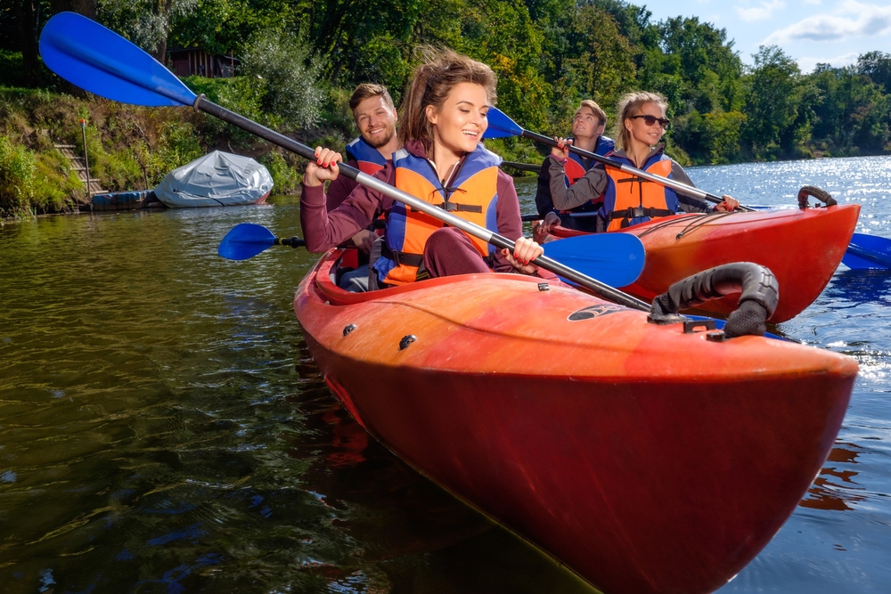 Freinds canoeing on a river then are wearing life jackets and their are trees around the river.  