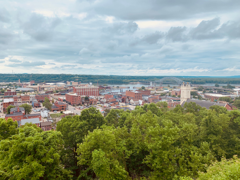 view of a city with red houses and buildings, a bridge, and green trees things to do in dubuque