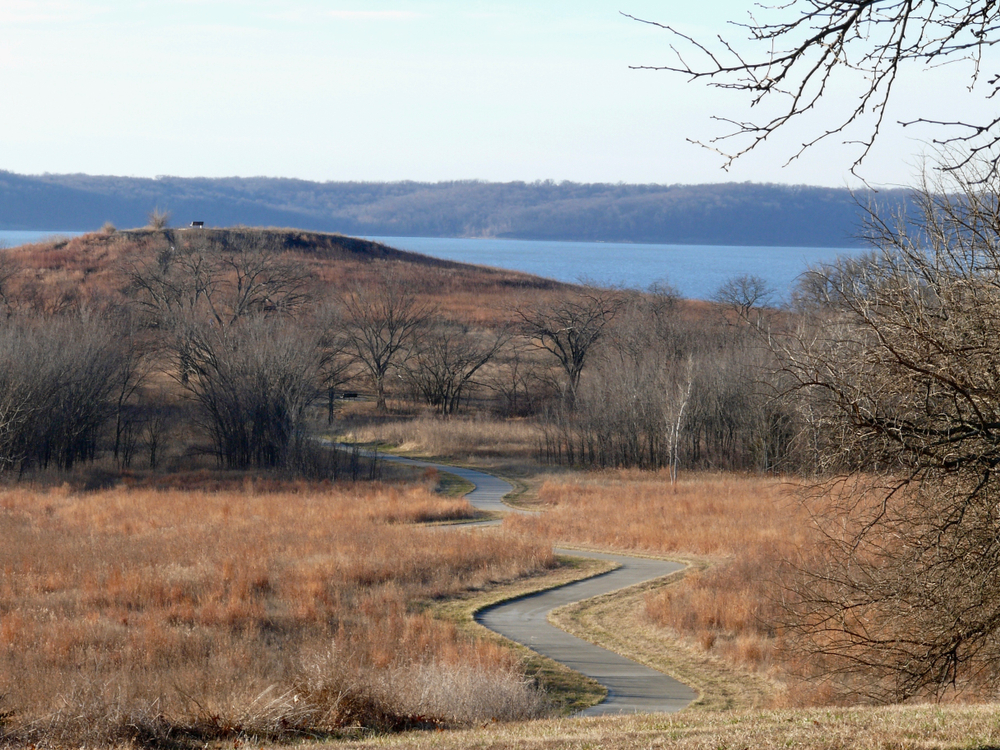 a trail winding towards a small hill and a lake things to do in lawrence
