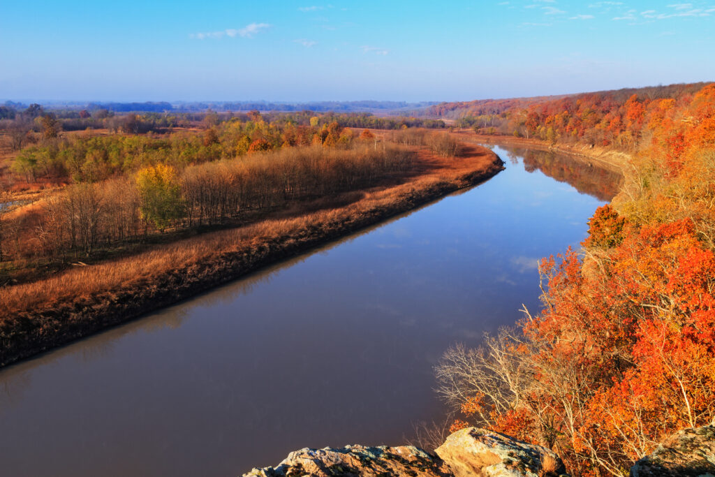 Brilliant orange leaves on trees on either side of blue river. Fall in Midwest