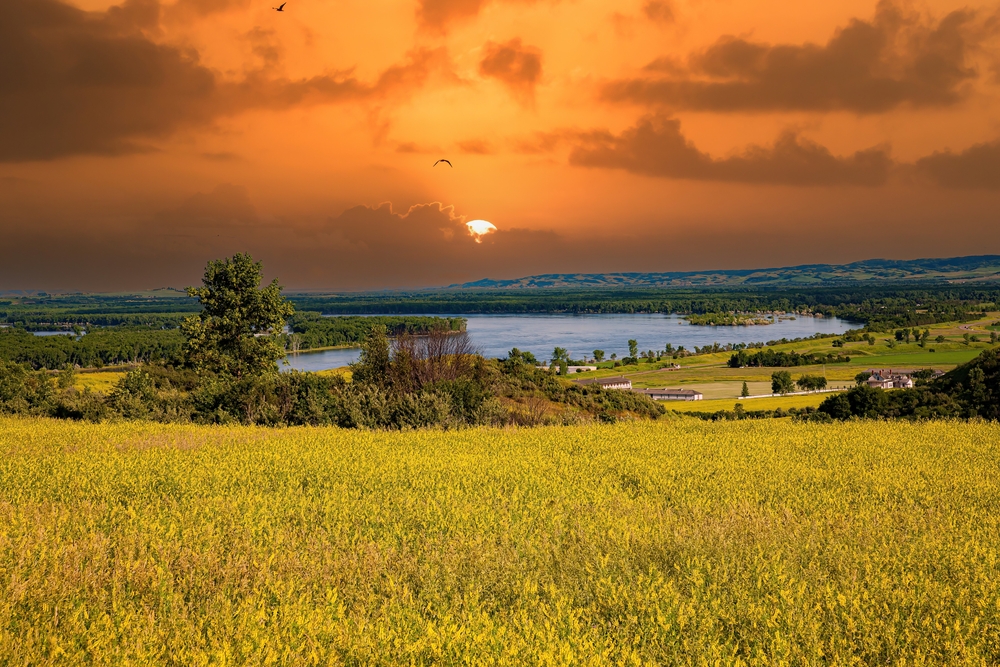 Sunset over the yellow prairie of Fort Abraham Lincoln State Park with a river in the distance.