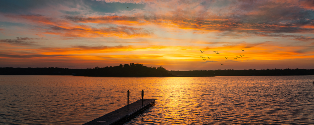 Orange sunset over Lake Metigoshe featuring a dock and flying birds during fall in North Dakota.