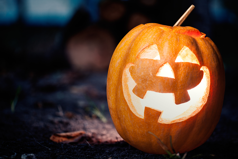 A smiling jack-o-lantern on a forest floor at night.