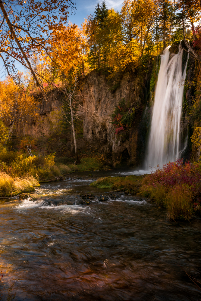 Spearfish Falls cascades down among in a forest during fall in South Dakota.