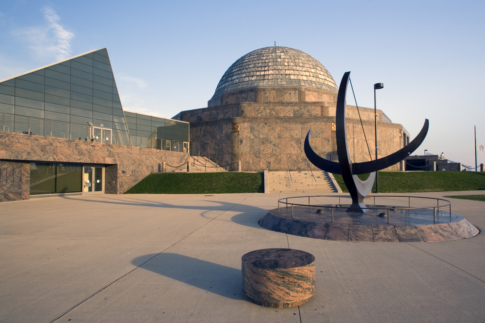 The exterior of the Adler Planetarium with courtyard that has a large sculpture in it. 