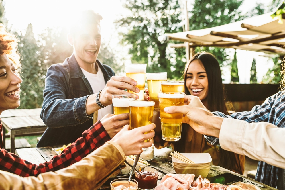 People clinking their glasses together on an outdoor patio on a sunny day, similar to what you'll find at breweries in Chicago