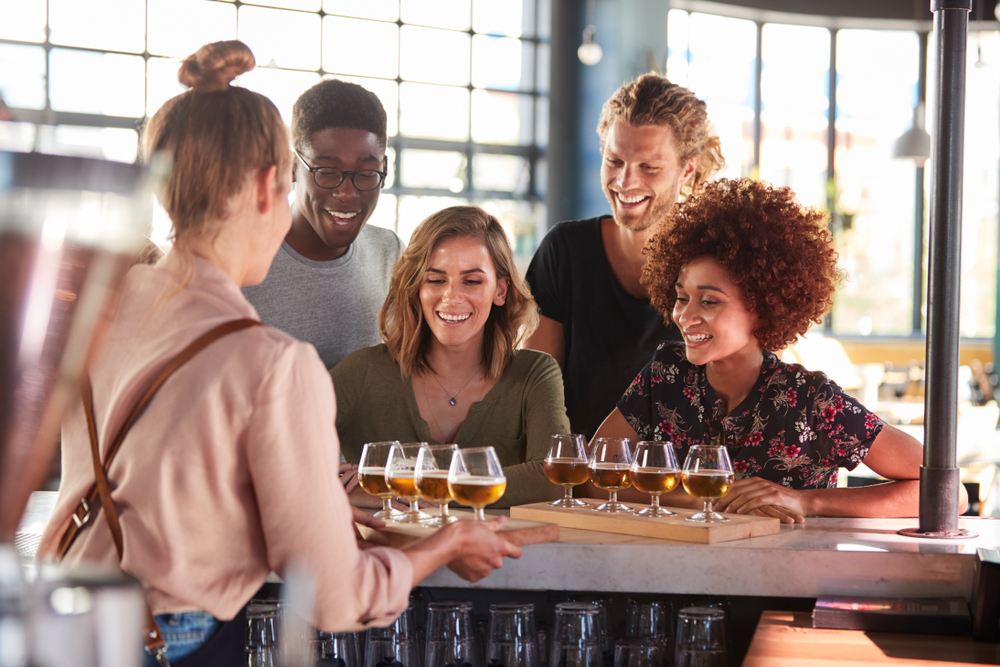 A group of people sitting at a bar similar to some breweries in Chicago while they get a private beer tasting in an industrial space.