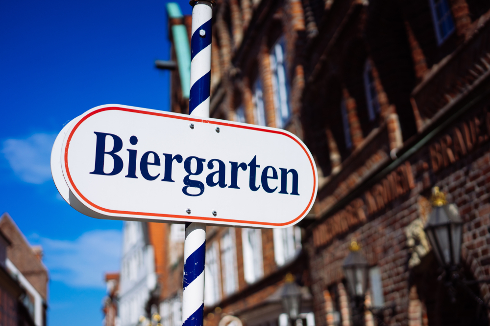 A sign outside of a large brick building that is a white oval and says 'Biergarten' in blue