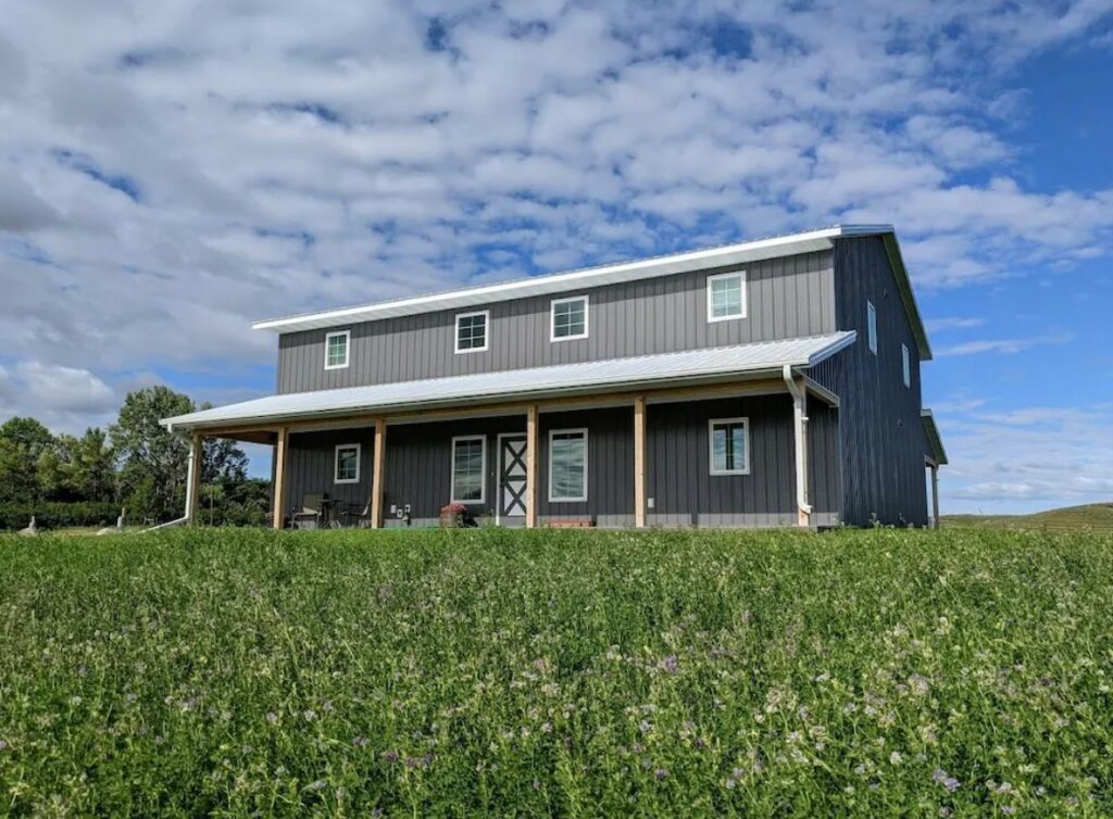 The front of a grey cabin in North Dakota surrounded by a field with purple flowers in it
