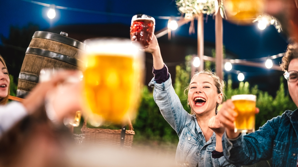 Happy woman clinking and toasting beer at brewery bar restaurant patio with friends. The article is about  breweries in Cleveland