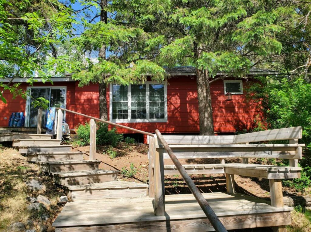 The front of a bright red cabin that is surrounded by trees with green leaves on a hill. There are steps leading up to the front door. One of the best cabins in North Dakota