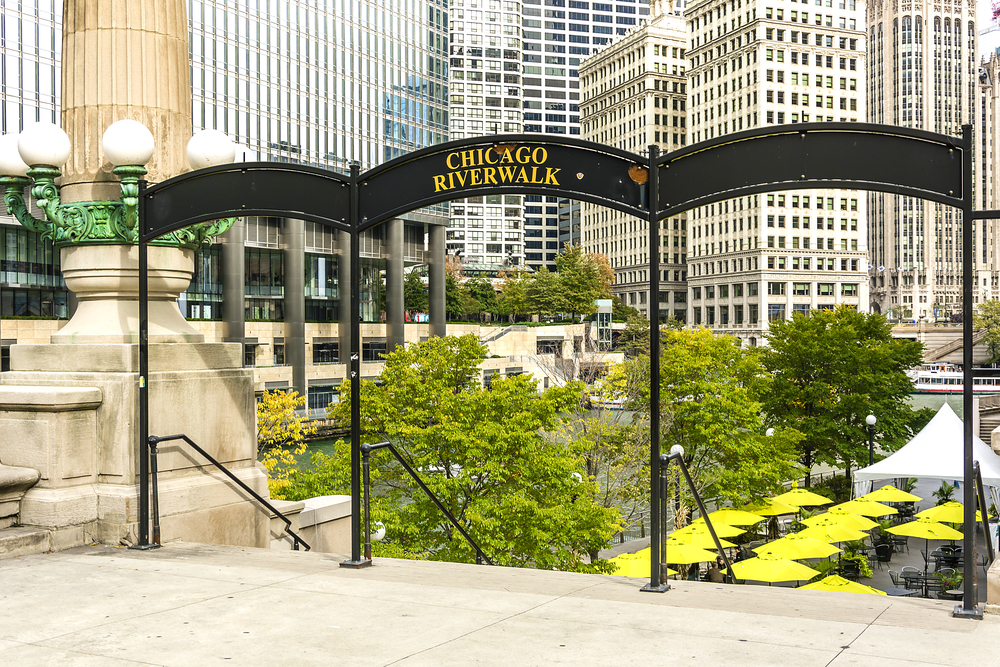 An entrance to the Chicago Riverwalk where there is an arching sign leading to steps down to the river in the middle of the city. See it during a weekend in Chicago
